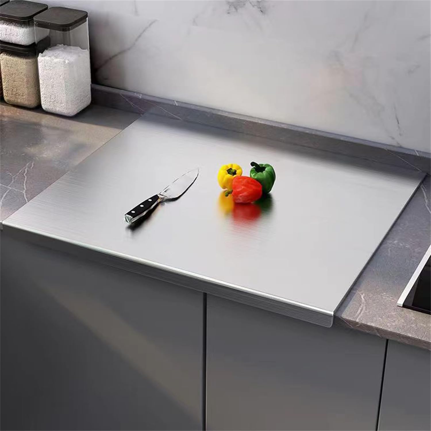 stainless steel Chopping board with a knife and colorful peppers on a kitchen counter.