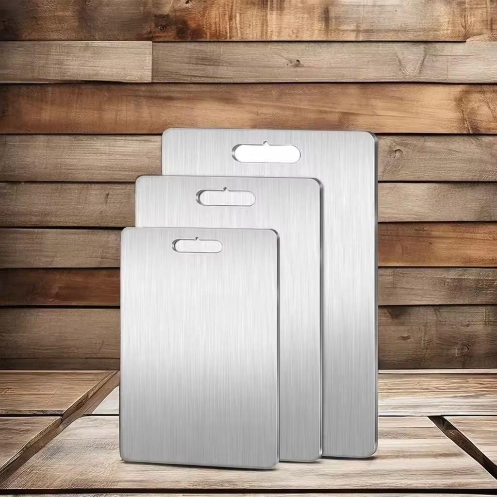 Three stainless steel cutting boards of different sizes on a wooden surface