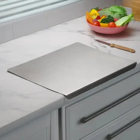 Stainless steel cutting board on a kitchen counter with a bowl of vegetables and a knife.